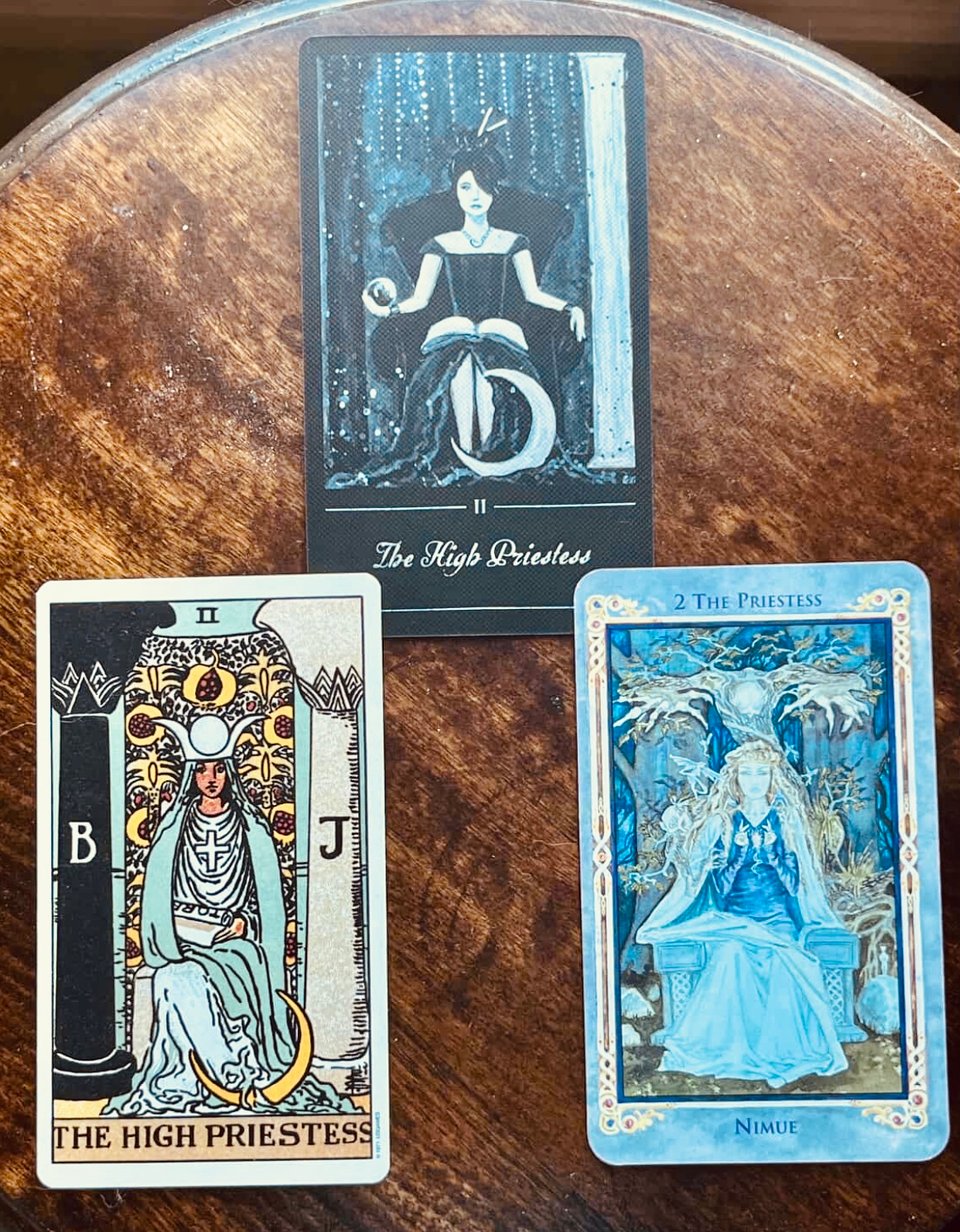 photo by Ali Trotta of 3 High Priestess tarot cards from different decks, on a wooden stool background