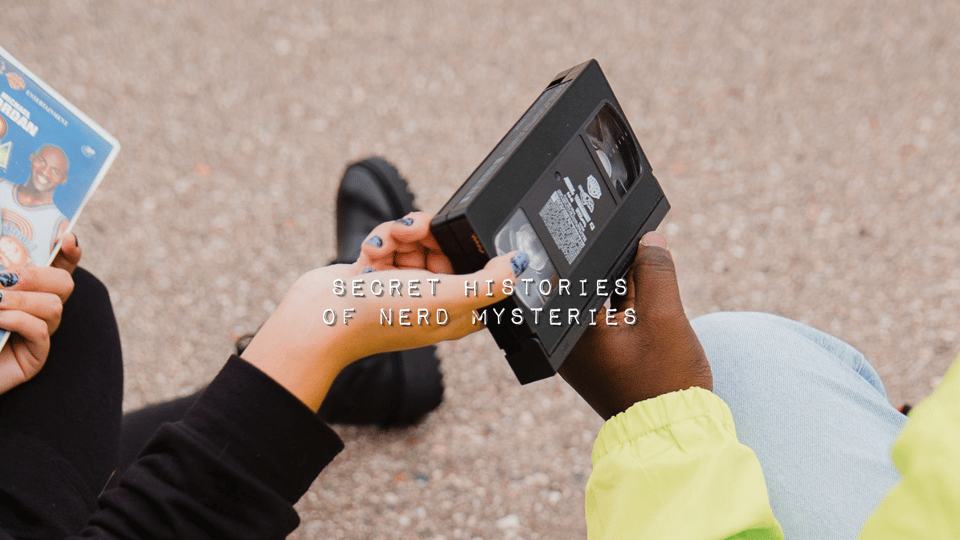 Brenda Snell's white hand and Austin Taylor's Black hand meet holding a VHS tape between their bodies as they sit beside each other on the ground. White typewriter text reads "Secret Histories of Nerd Mysteries" over the center of the image.