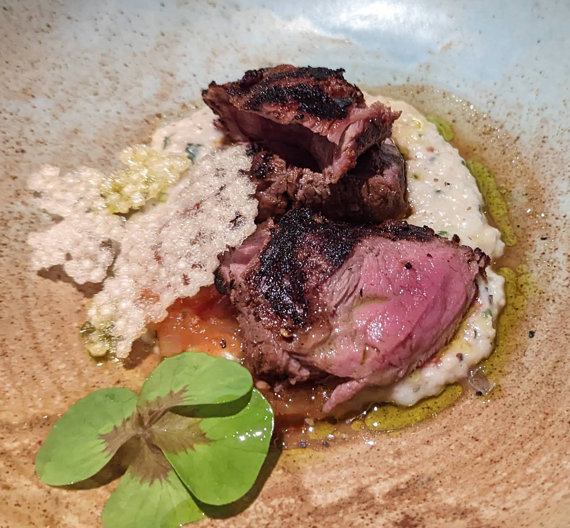 Wild boar tenderloin sitting on a grain mash with a crispy cracker and fresh microgreen garnish on top