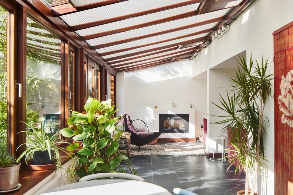 A large south-facing garden room. There's a run of hardwood windows with lots of plants on the left, and a slate floor.