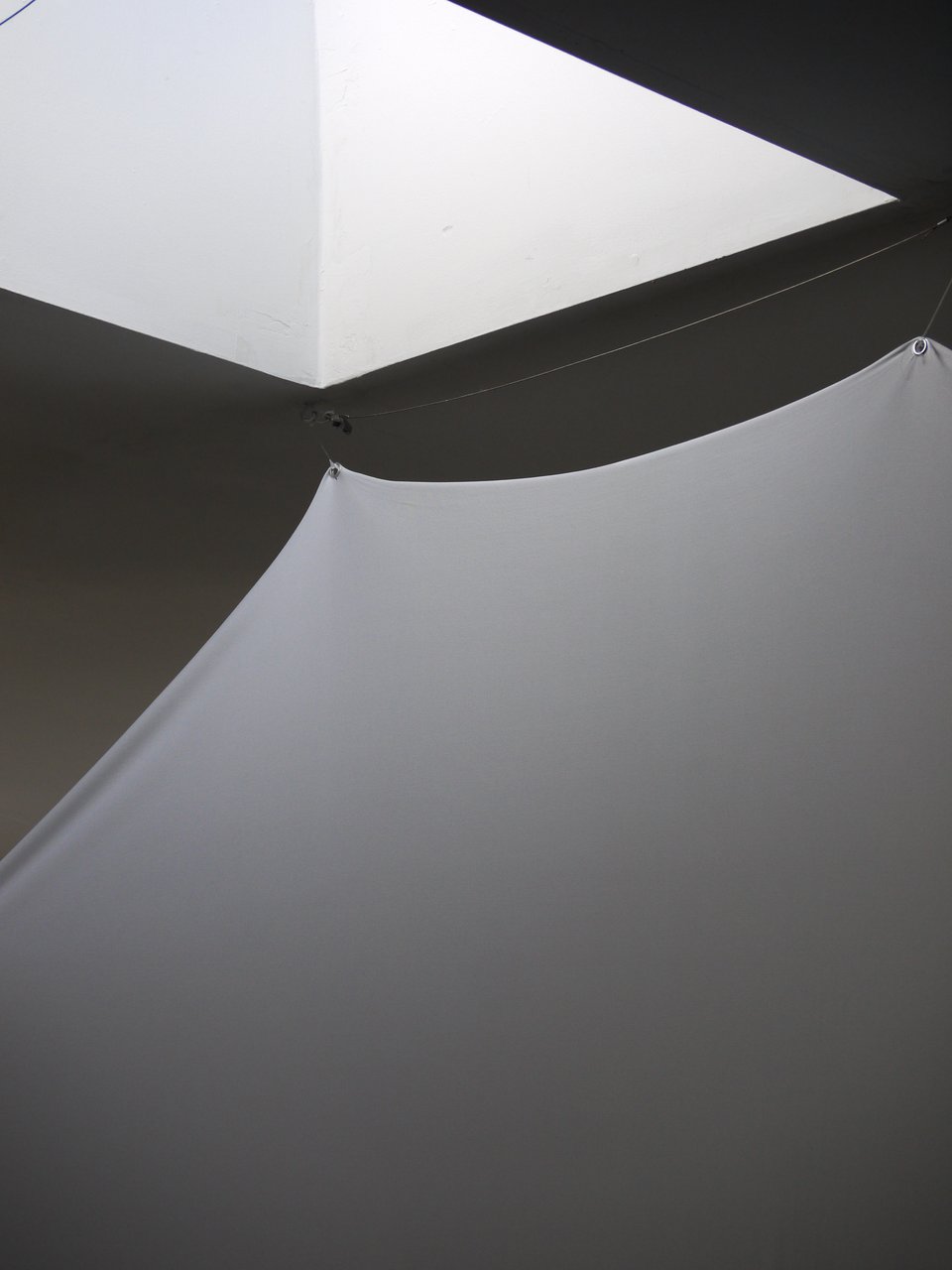 close-up of a stretchy white cloth suspended below a skylight. the top of the cloth is gently illuminated by indirect light.