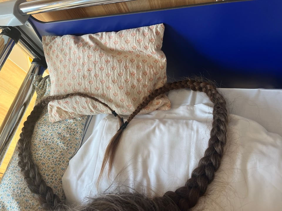 Two braids of brown hair form a heart on the pillow of a hospital bed.