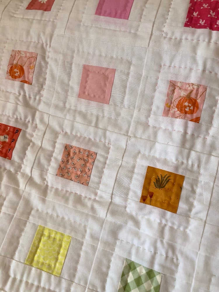 A close up look at the hand quilting on the scrappy quilt. The stitching goes around the outside of each square to form another square, and there's more stitching inside the main square to make a smaller square.