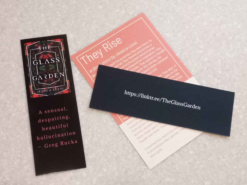 A bookmark featuring the cover art for THE GLASS GARDEN, and a postcard-sized paper with a short story on it.