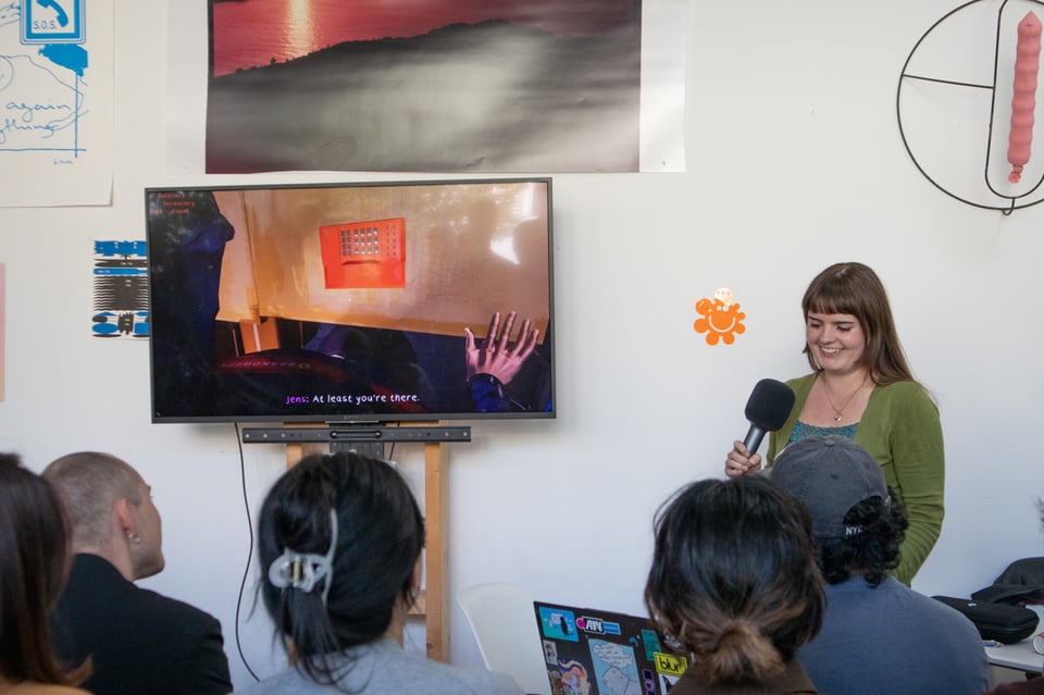 A presenter dressed in green and blue smiles as she presents in front of a crowd