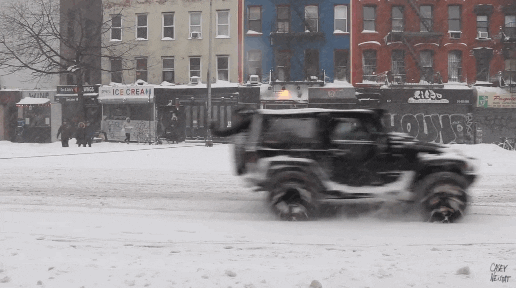 A mildly crazy or extremely brave person on a snowboard being towed by Jeep at speed in NYC