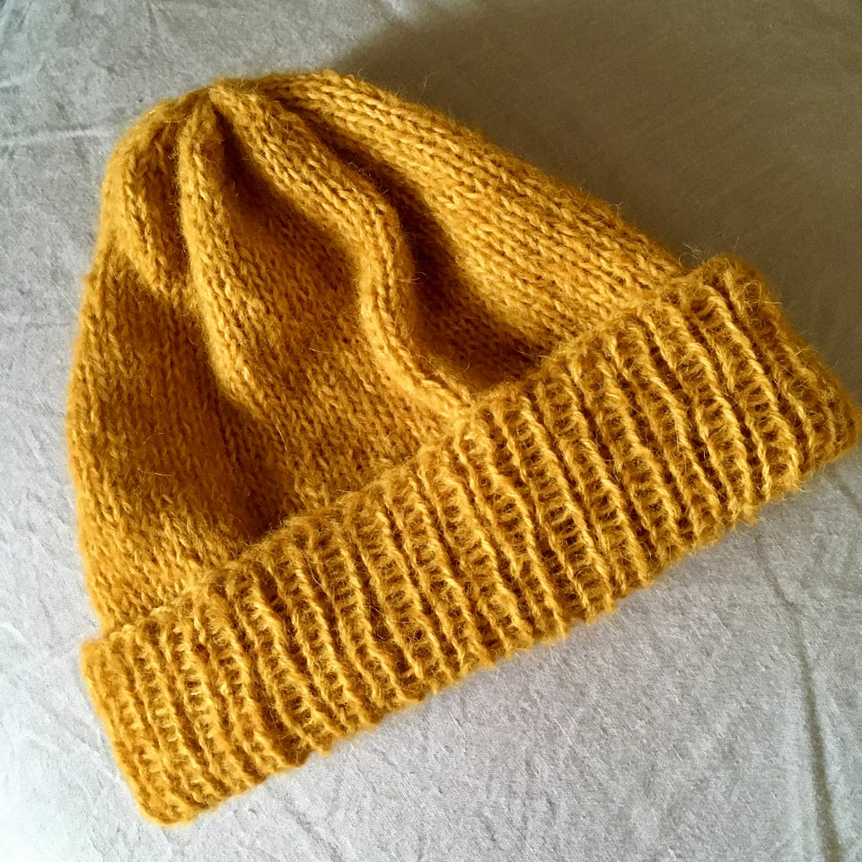 A hand knitted woollen hat in a warm gold colour.