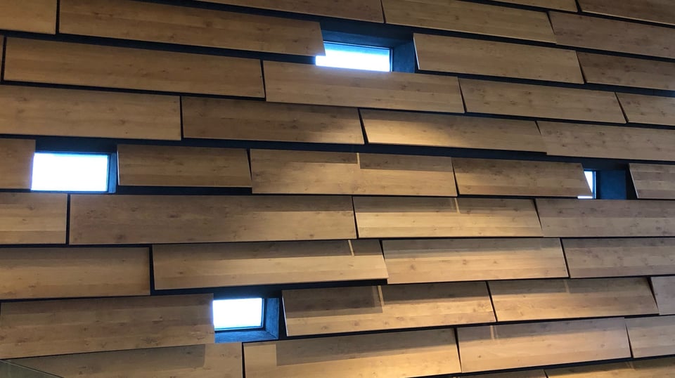 A photograph of the interior of the V&A Museum in Dundee. It shows a section of wall that is clad in horizontal planks of wood. At various intervals there are windows that are equal in height to the planks but shorter in width.