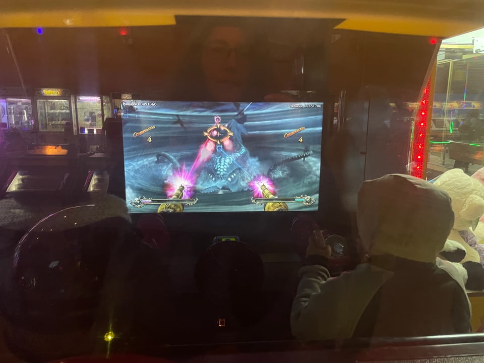 Two people are seen from behind playing a video game shooting at a Kraken squid.