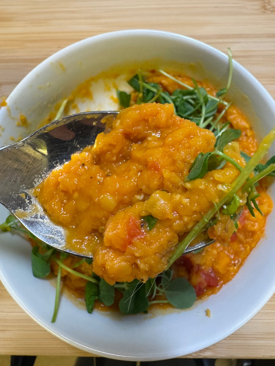 A white bowl filled with golden colored red lentils, pea shoots, diced tomatoes, and spices.