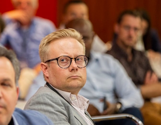 Head and shoulders of Andreas Wassberg, sitting in a business conference, listening. Blurry faces of other delegates around him.
