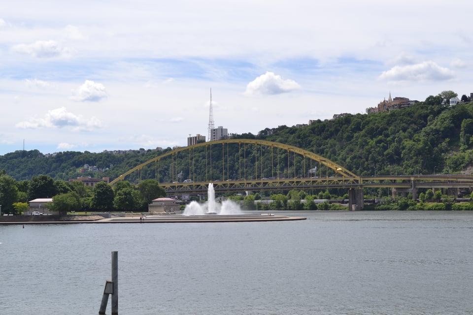 A river with a fountain projecting out into it and a bridge beyond.