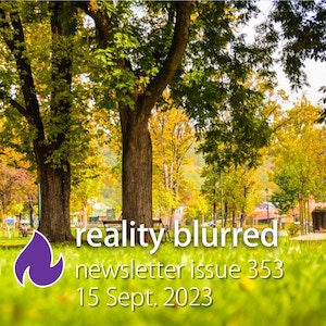 A park with bright green grass and two trees in the foreground; in the background, other trees have orange leaves