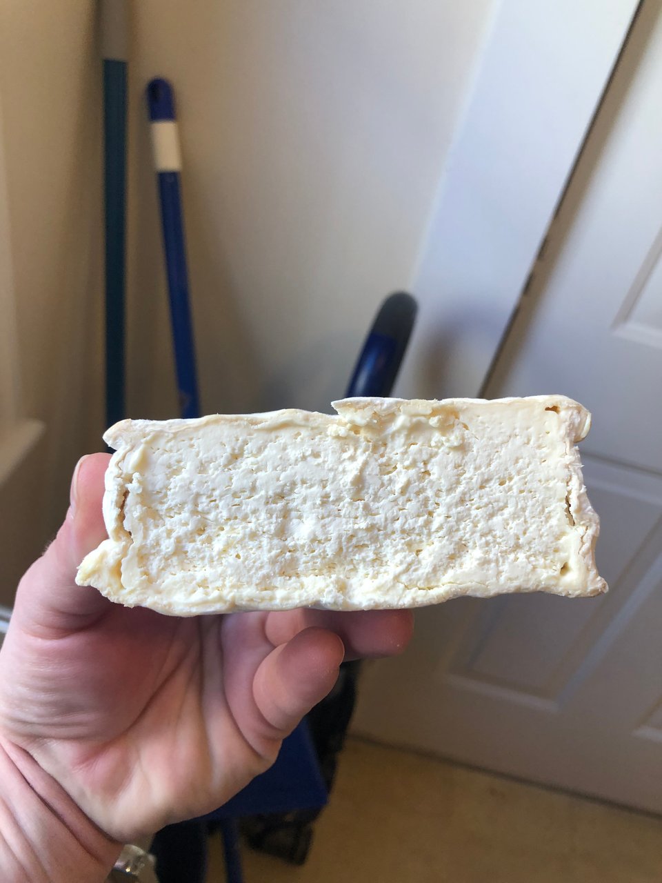 a half cheese being held aloft by a pink hand, showing a clear rind but not a clear cream line. This cheese does not have a coherent curd.