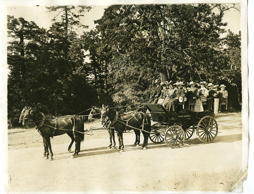 Sepia coloured photo. About 15 passengers aboard a carriage being pulled by 4 horses.