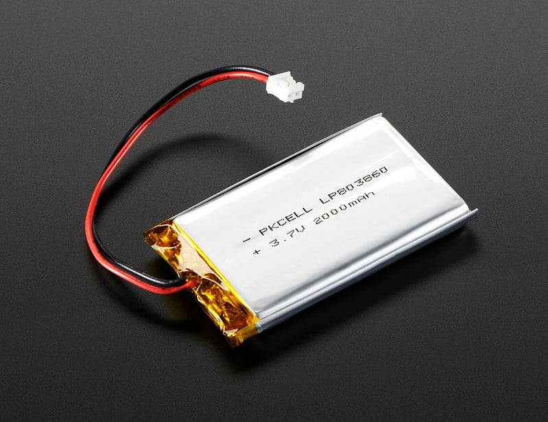 A picture of a small lithium ion battery, silver cololred with a copper colored end, and two wires -- red and black -- protruding, ending a white plug-style ending