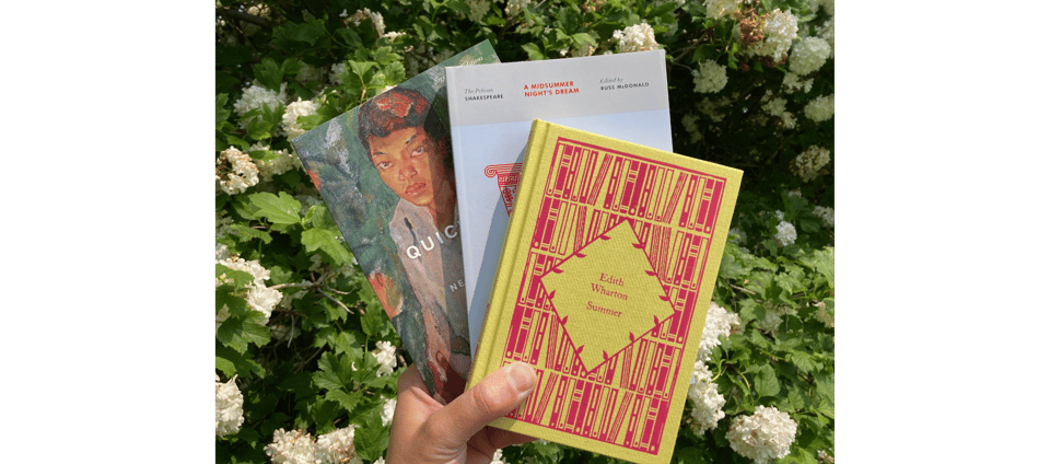 a hand holding the three books described below in front of a flowering bush