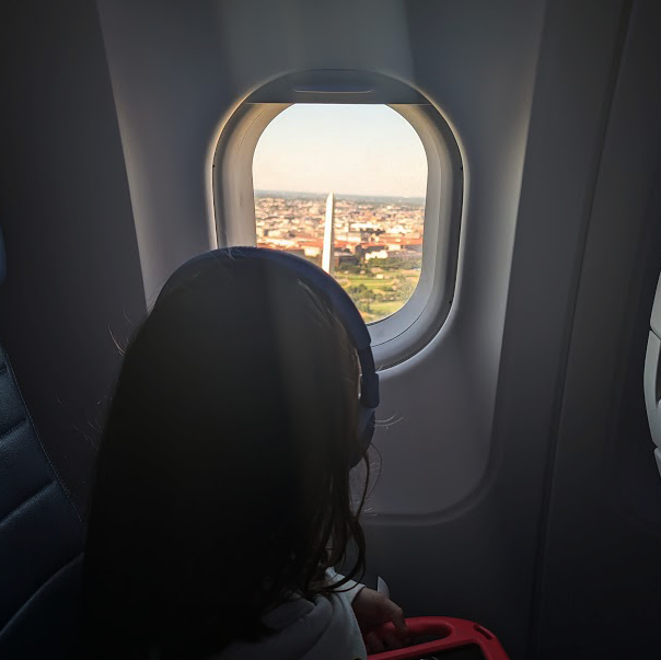 A small child looks out an airplane window at the Washington Monument
