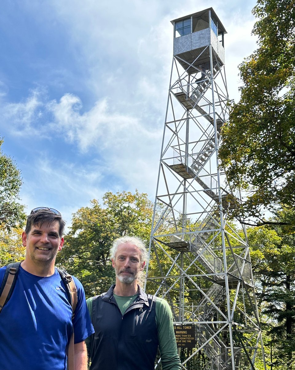 Photo of two white men in front of a fire tower in the woods