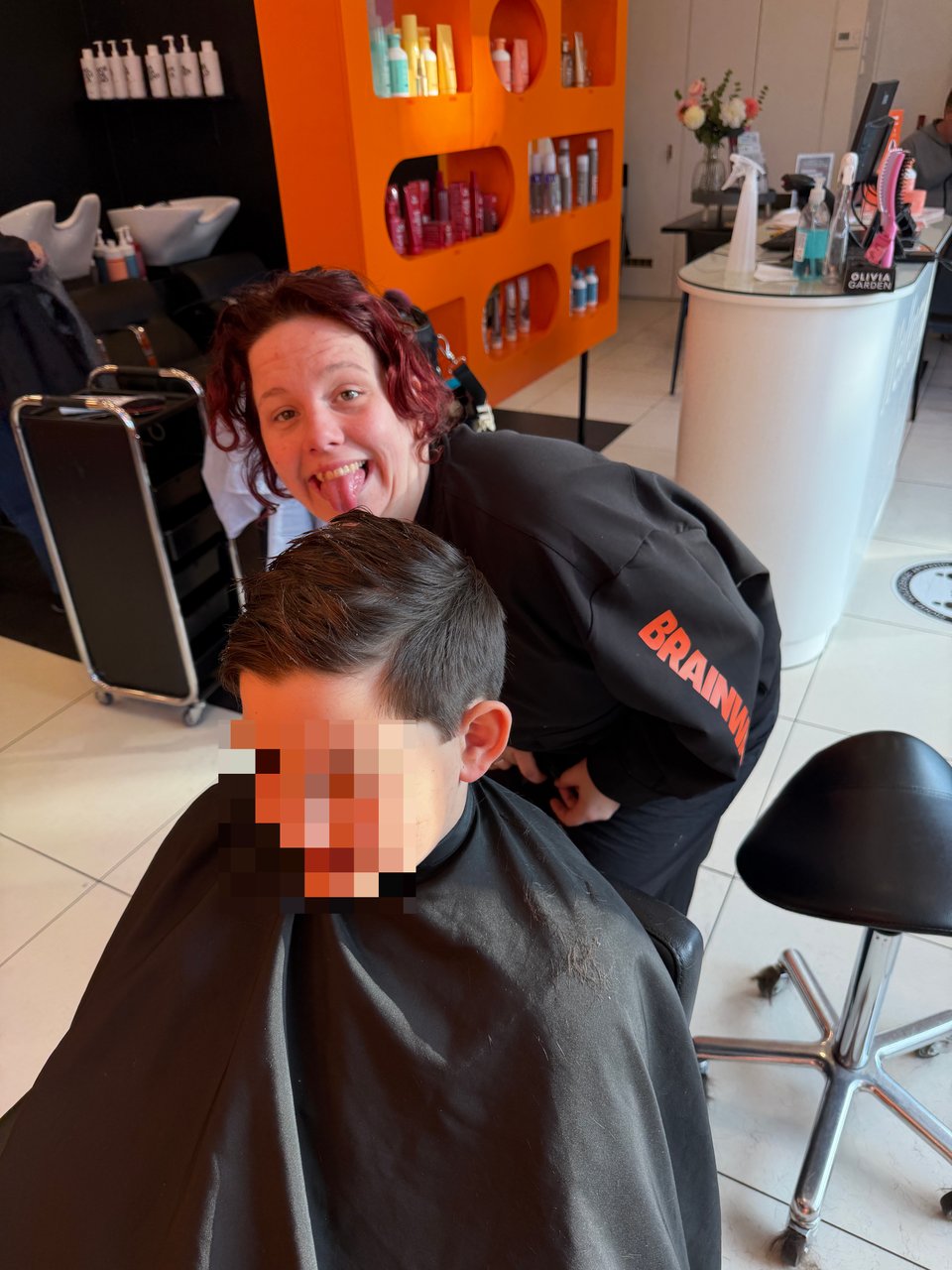 A young boy is getting his hair cut and the stylist makes a funny face behind him.