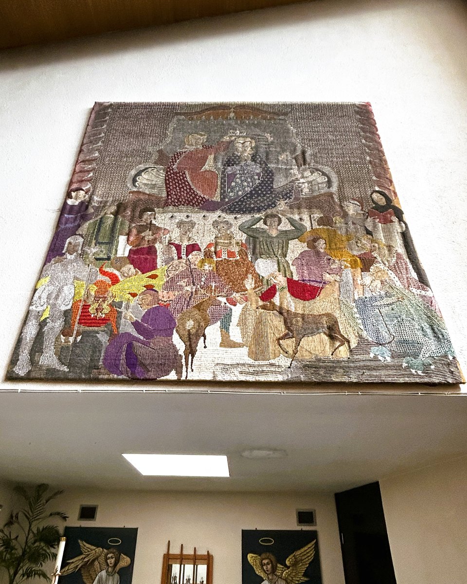 A huge tapestry hanging high on a plain wall. It shows the consecration of Mary, and has fourteen other saints stood around her. It looks oddly modern whilst also being clearly inspired by pre-Renaissance art.