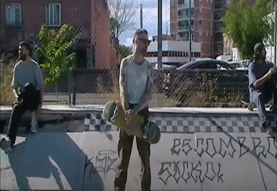A screen shot of a music video showing a man holding a skateboard