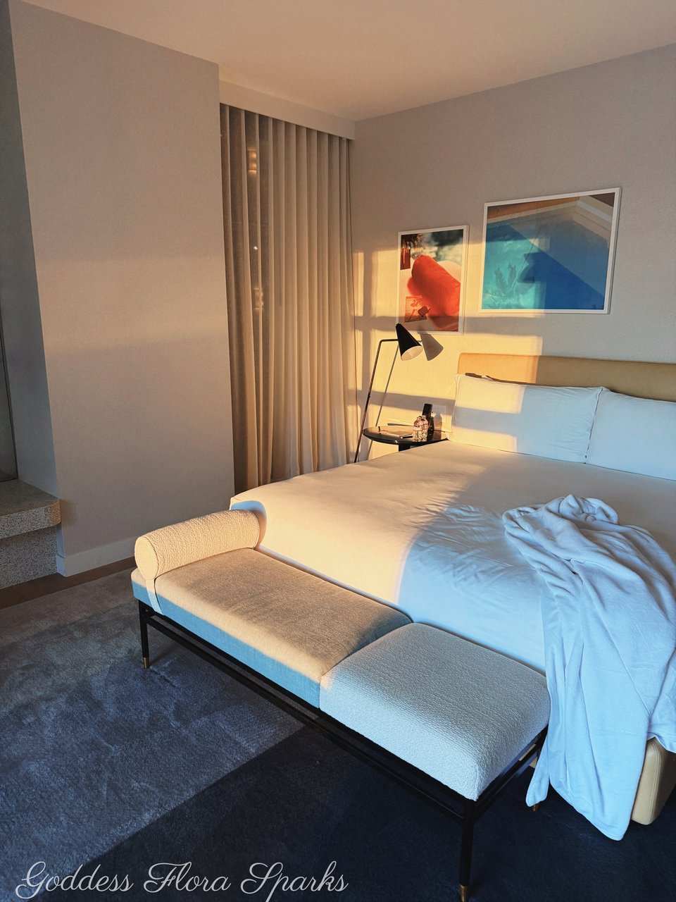 picture of a hotel bed. A white hotel robe is on the bed, some bright light is shining in onto the bed