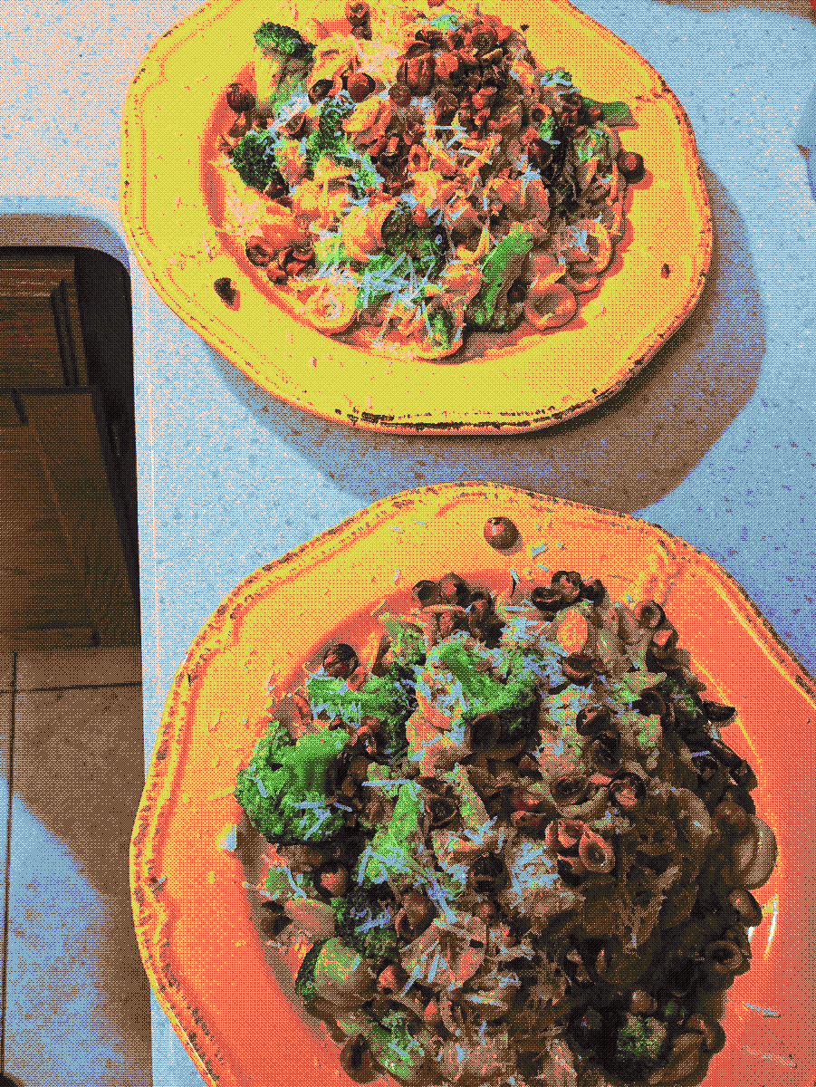 Two yellow plates loaded with pasta and broccoli, topped with grated cheese and hazelnuts. Photo with a dithering effect applied.