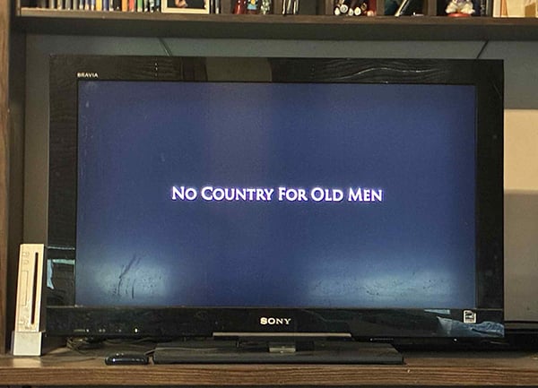 A television with a blank screen and the words No Country for Old Men in white letters