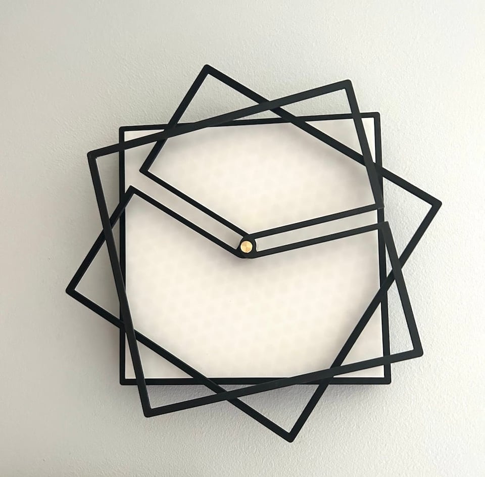 A wall clock that has a black square frame. On top of the frame are two black squares nearly the same size as the frame -- only slightly larger. In each of these two squares, there is one wall of the square that has two pieces jutting inwards towards the center of the clock face. These arms connect to the clock motor in the center. One of the squares has its arms pointing at 10 o'clock; the other is pointing at 2 o'clock. The visual effect is thus of two squares stacked on top of the bottom one, at varied angles from the bottom one