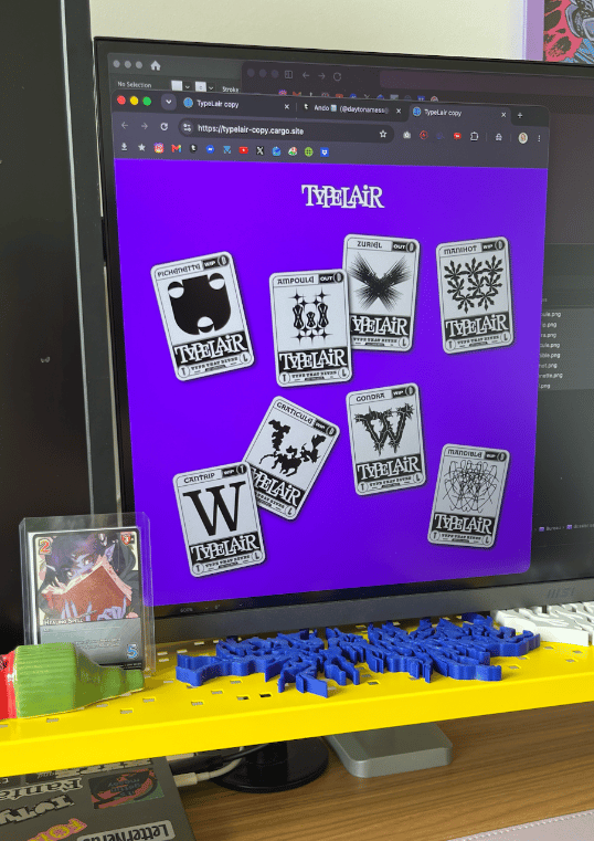 Photos of my setup with a website showing. Purple background, with a few trading card game looking cards on it, except the cards are showing letters in different typefaces.