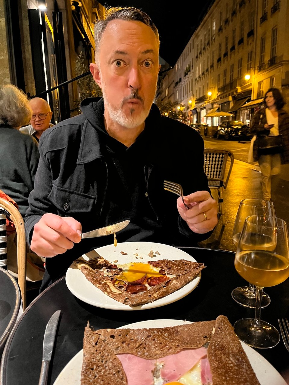Matt on a parisian street, outside a cafe, eating a savory buckwheat crepe