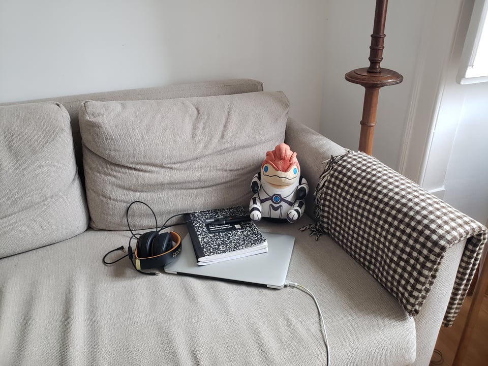 my laptop on a sofa with my headphones and my emotional support krogan