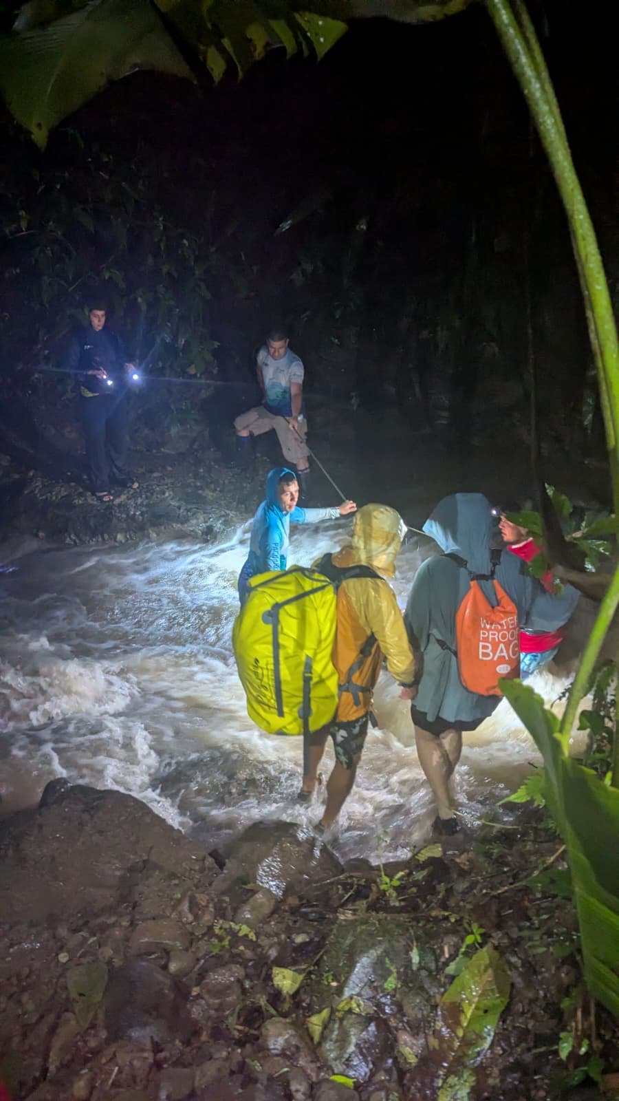 An image of hikers' backs as they cross a large river in the dark.