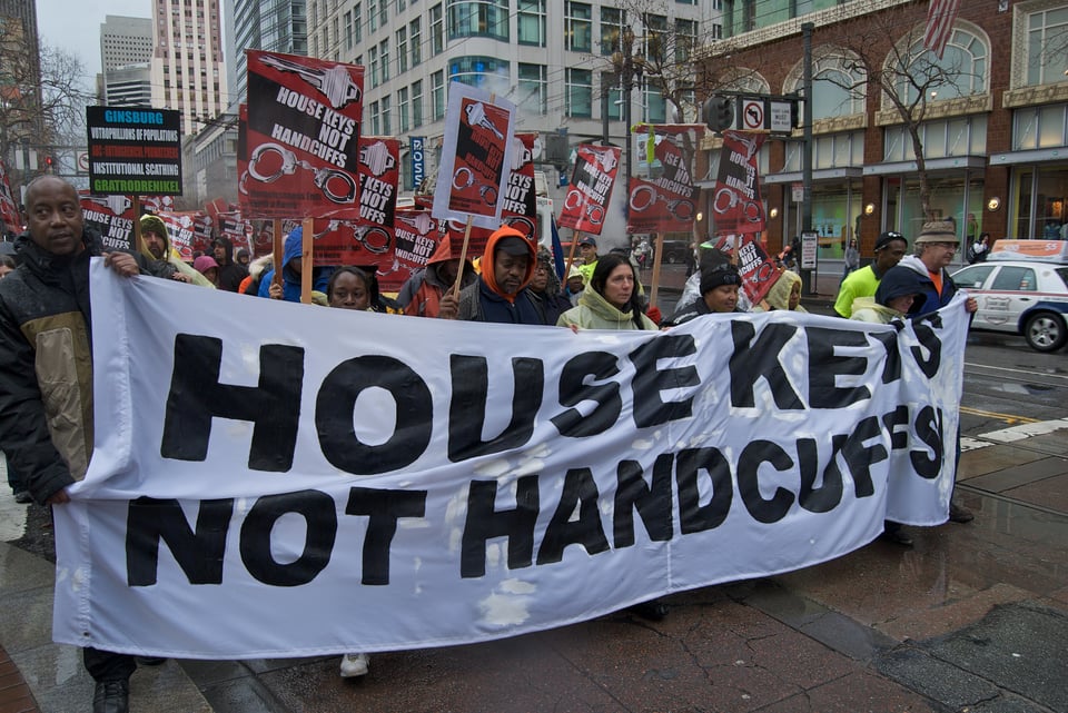 A protest on Market Street in San Francisco featuring people marching with signs that say HOUSE KEYS NOT HANDCUFFS, plus a banner that says the same thing.