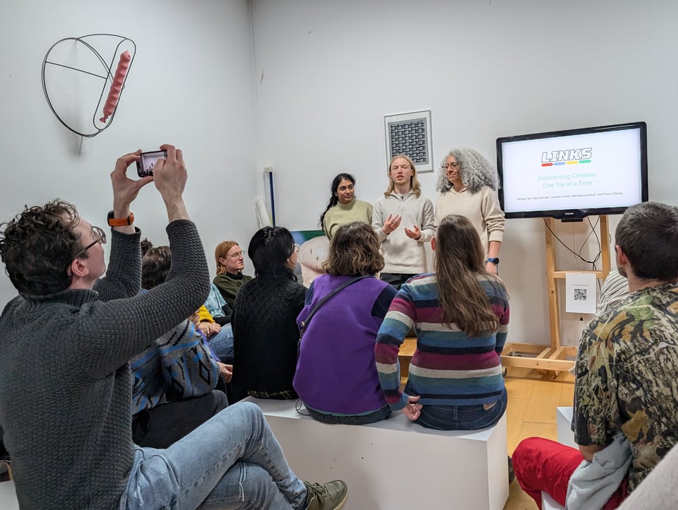 a group of people in a room listen to three speakers presenting their card game "Links"