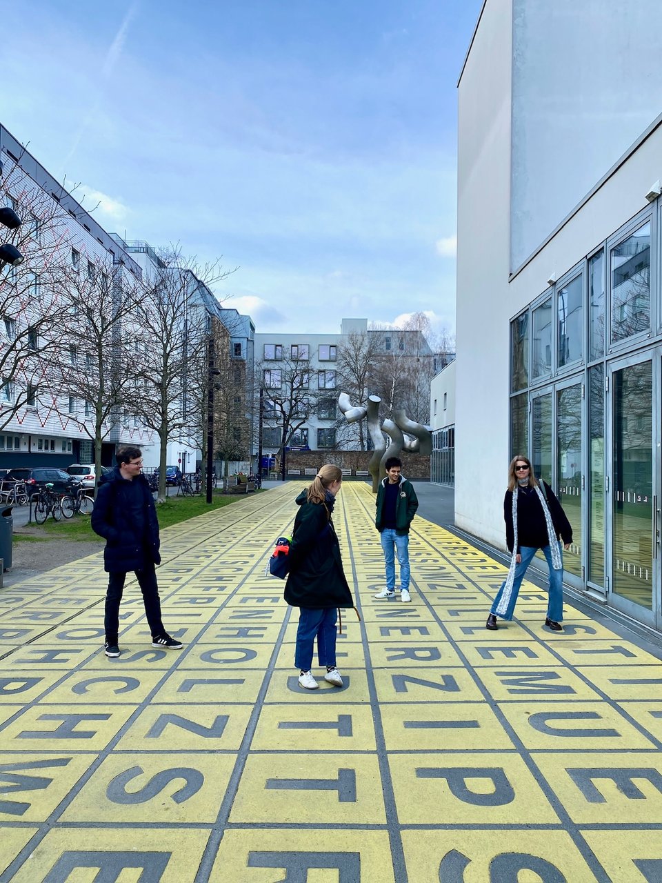 Four of us standing outside Berlinische Galerie, on a bunch of letters displayed on the ground