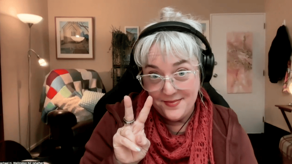 Rachael giving peace sign, smiling prettily, red scarf, white hair, glasses