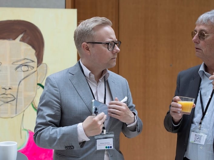 Two men speaking together in a conference venue, with lanyards around their necks. The man on the left is Andreas Wassberg.