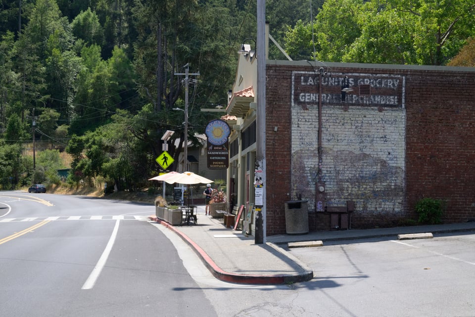 Lagunitas grocery store sign painted on the side of a building, next to a two lane road.