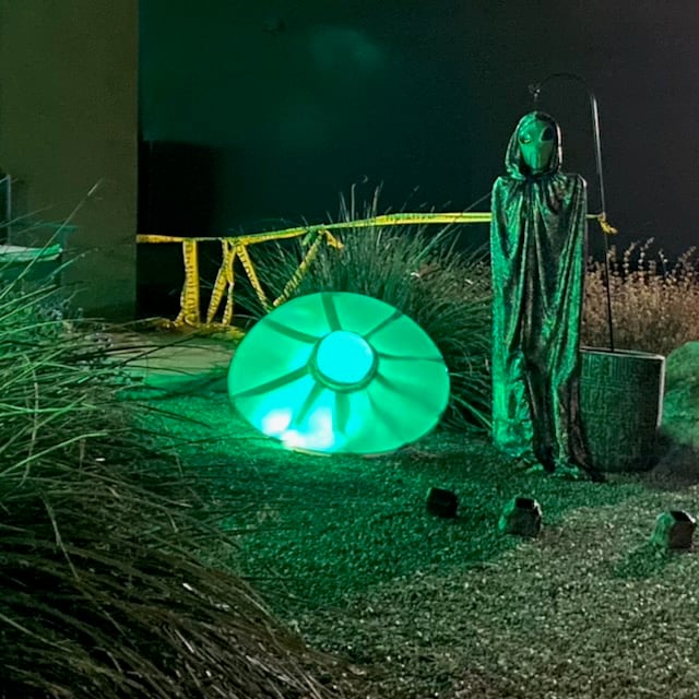 front yard with diy crashed ufo and tall alien wearing a clock next to it.