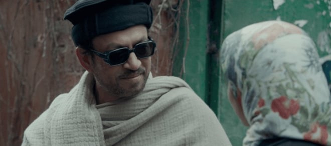 Irrfan Khan in Haider wearing sunglasses, slightly smiling and talking to a woman.