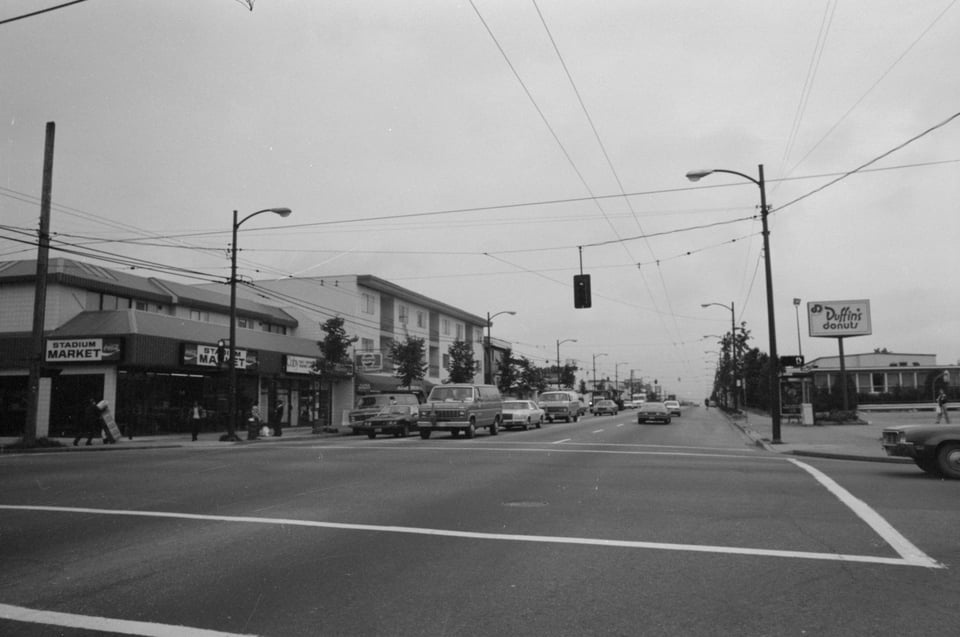 Black and white street scene showing businesses. You can see Stadium Market on the left and Duffin's Donuts on the right.