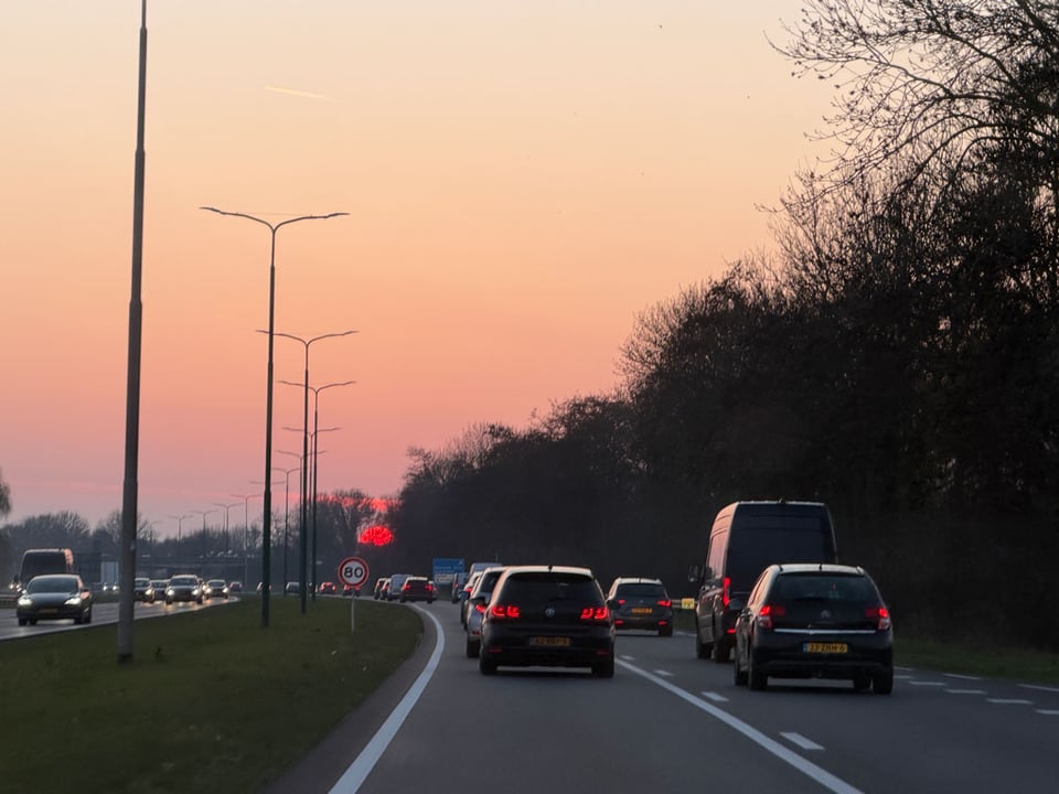 The red sun shines off in the distance at the end of the freeway.