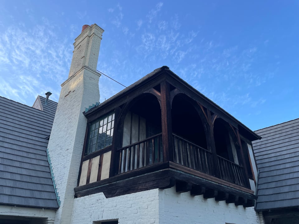A view of a small wooden balcony and a brick chimney reaching toward a beautiful blue sky