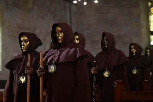 A group of hooded people wearing gold masks in a church