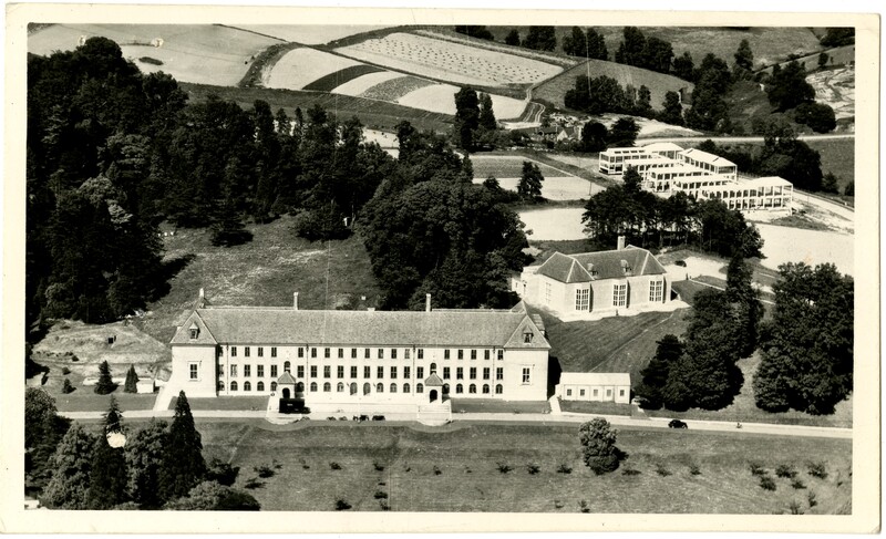 An aerial shot with three buildings visible on what is otherwise a slope of fields and trees.