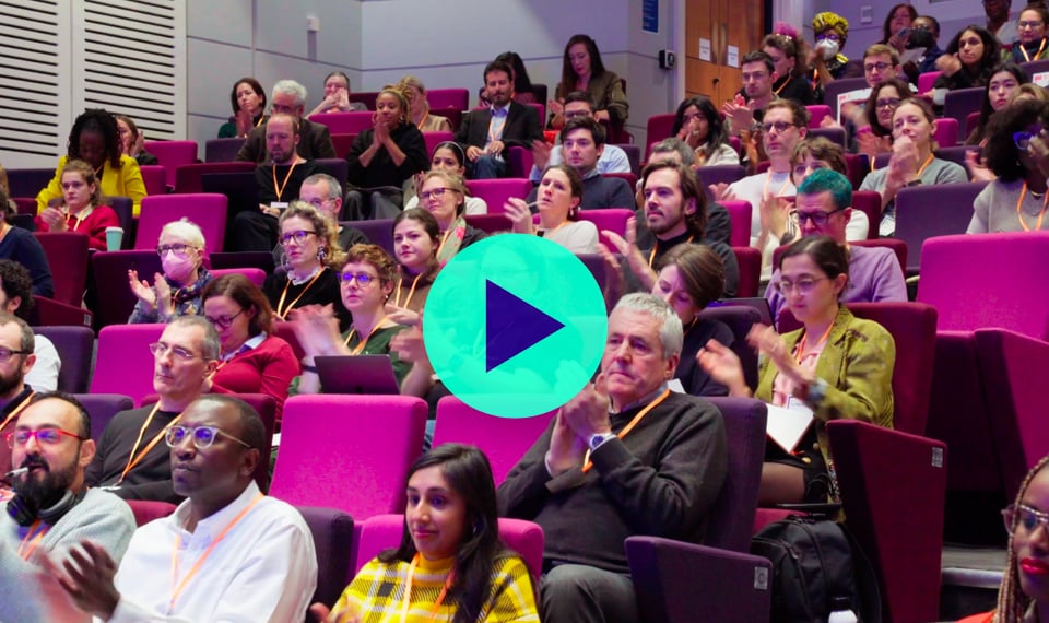 A picture of a group of people in a rake auditorium with a video playbutton in the middle