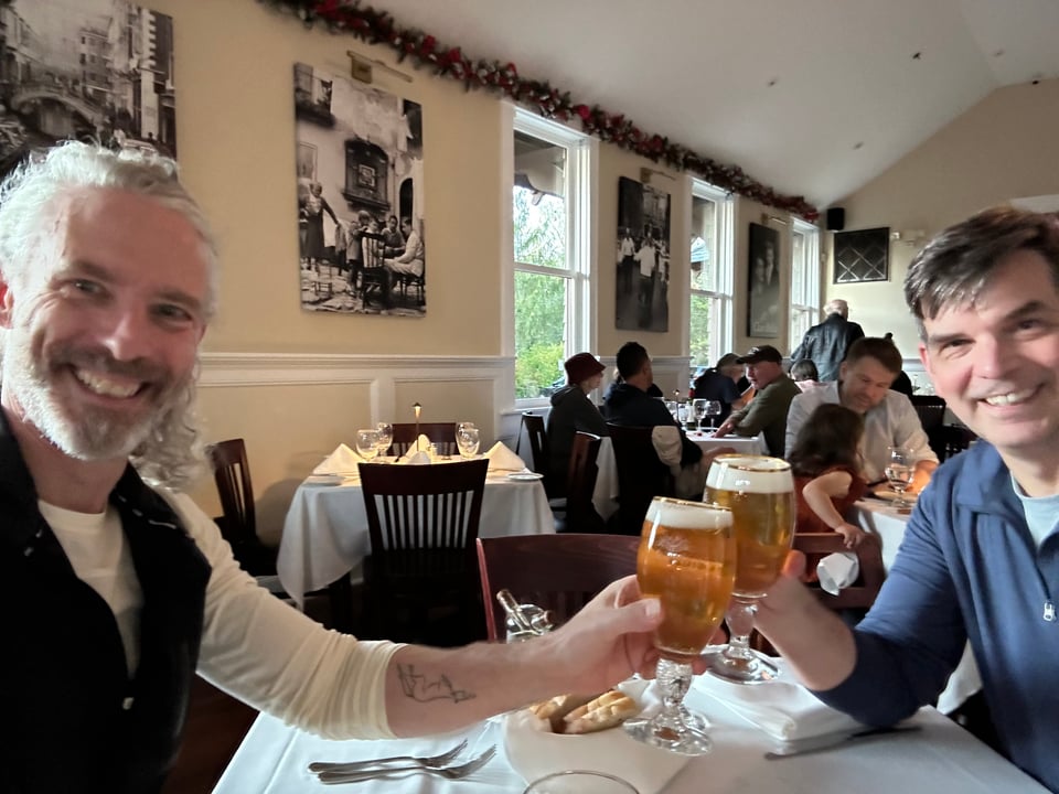 Two white men clinking Stella Artois pint glasses of beer in a restaurant