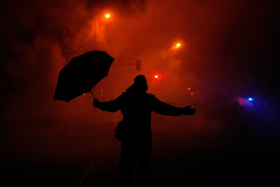 A protester holds an umbrella as they react to tear gas after a shooting on Jan. 14, 2026, in Minneapolis.